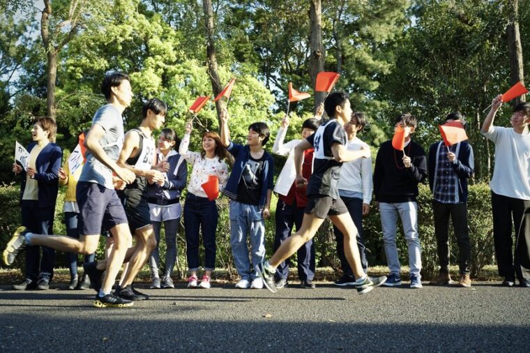 กองเชียร์ถือธงสีแดงโบกให้กำลังใจนักวิ่งริมถนนในงานมาราธอนที่เกียวโต